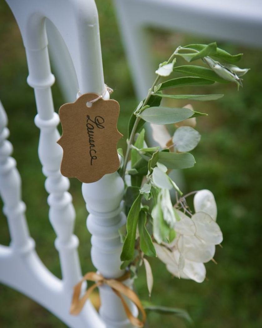 Étiquette de bois et brin de verdure noués au dossier d’une chaise blanche
